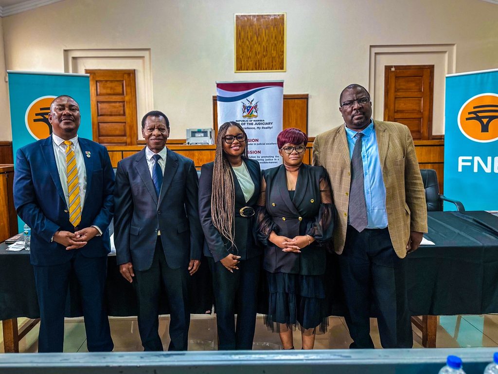 WhatsApp Image 2026-10-02 at 30528 PM - The Brief | Namibia's Leading Business & Financial News Five professionals in formal attire posing for a photo in a conference room, with banners in the background on either side.