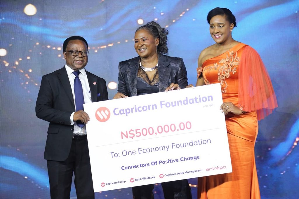 WhatsApp Image 2026-10-05 at 102108 AM - The Brief | Namibia's Leading Business & Financial News Three people at an award ceremony holding a large check from Capricorn Foundation for ₦500,000 to One Economy Foundation, smiling on stage.
