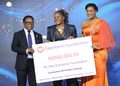 Three people at an award ceremony holding a large check from Capricorn Foundation for ₦500,000 to One Economy Foundation, smiling on stage.