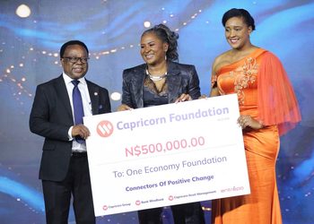 Three people at an award ceremony holding a large check from Capricorn Foundation for ₦500,000 to One Economy Foundation, smiling on stage.