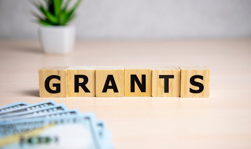 Wooden letter blocks spell 'GRANTS' on a desk with money in the foreground.