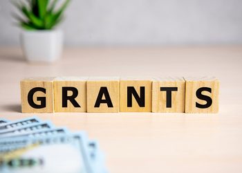 Wooden letter blocks spell 'GRANTS' on a desk with money in the foreground.