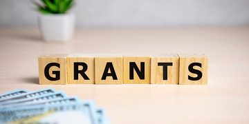 Wooden letter blocks spell 'GRANTS' on a desk with money in the foreground.