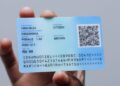 Blue citizen ID card being held, featuring a QR code and printed personal details on a light background