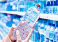 Person holding a clear plastic water bottle with a red cap in a grocery store aisle of bottled water on shelves.