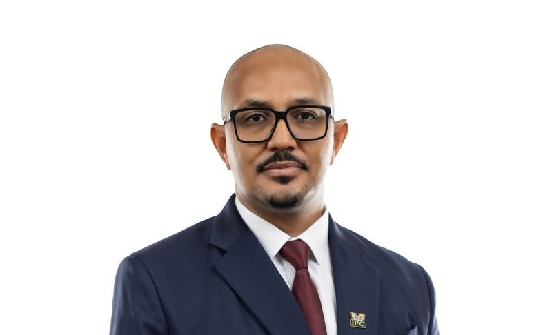 Professional head-and-shoulders portrait of a bald man with black glasses, in a navy suit and red tie.