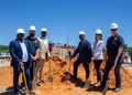 Pupkewitz Megabuild - The Brief | Namibia's Leading Business & Financial News Group of seven professionals in hard hats with shovels at a daytime groundbreaking ceremony on an orange dirt site, with a brick wall and vehicles in the background.