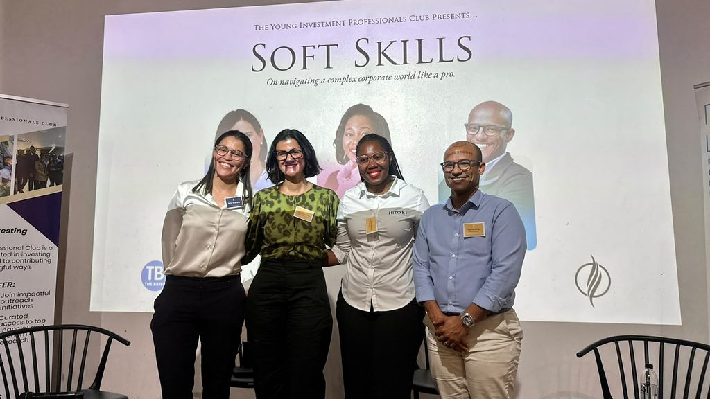 Four professionals pose and smile for a group photo on a stage in front of a large 'Soft Skills' banner at a conference event.