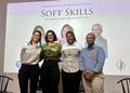 Four professionals pose and smile for a group photo on a stage in front of a large 'Soft Skills' banner at a conference event.