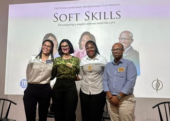 Four professionals pose and smile for a group photo on a stage in front of a large 'Soft Skills' banner at a conference event.