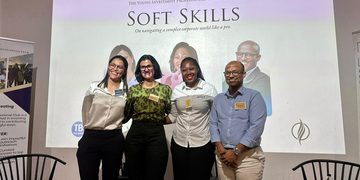 Four professionals pose and smile for a group photo on a stage in front of a large 'Soft Skills' banner at a conference event.