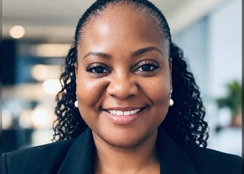 Smiling Black woman in a black blazer with pearl earrings, in an office setting (close-up portrait).