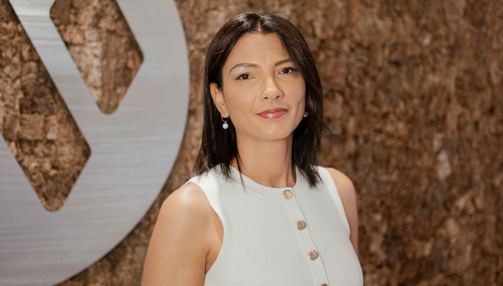 Portrait of a woman with dark hair wearing a light sleeveless dress, posing at an event.
