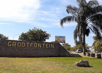 Stone wall sign reading 'GROOTFONTEIN' at the entrance with a palm tree and grassy area nearby.