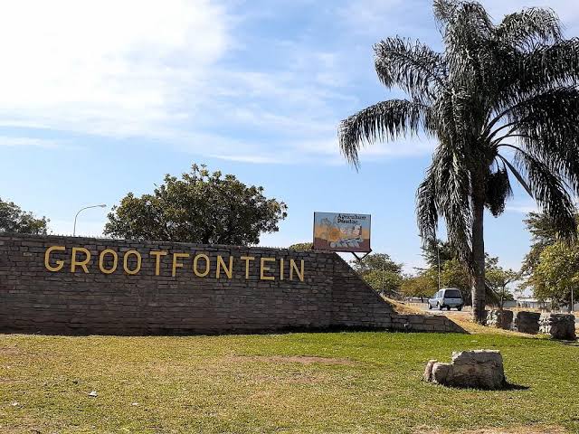 Stone wall sign reading 'GROOTFONTEIN' at the entrance with a palm tree and grassy area nearby.