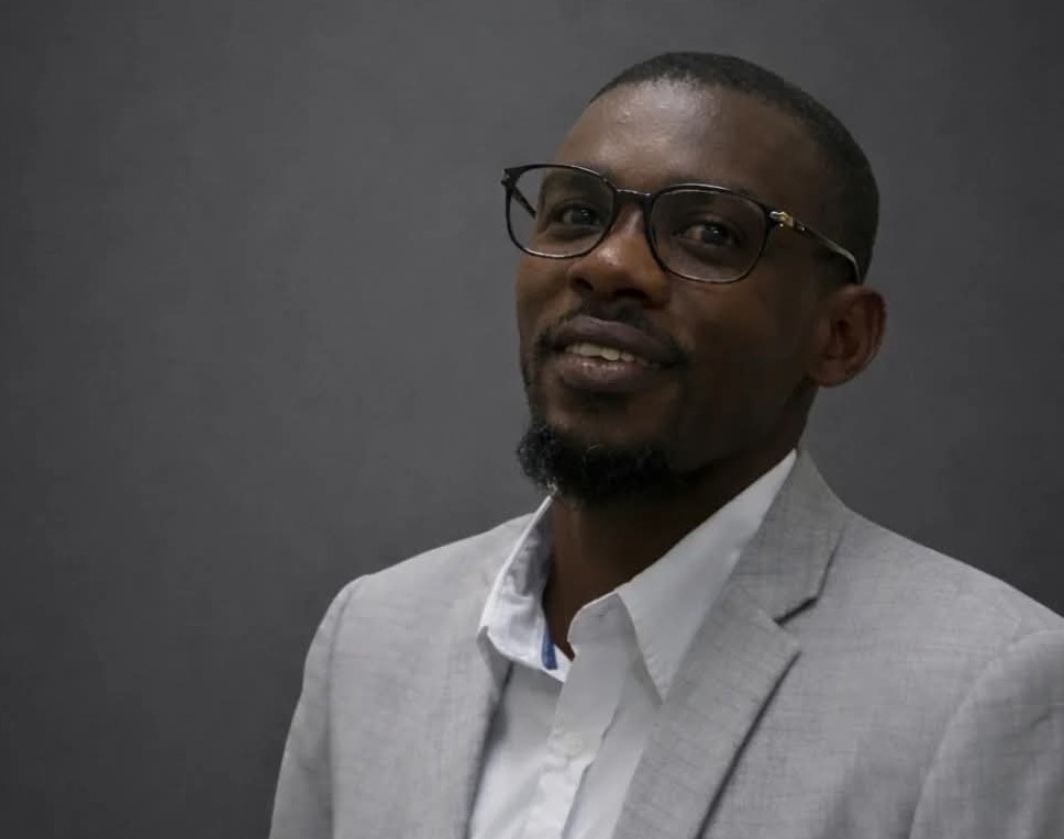 NOAH - The Brief | Namibia's Leading Business & Financial News Head-and-shoulders portrait of a man in a light gray suit and white shirt, wearing glasses, smiling slightly.