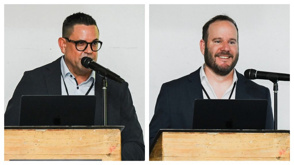 MixCollage-12-Oct-2026-12-16-PM-3590 - The Brief | Namibia's Leading Business & Financial News Two men in suits speak at separate wooden lecterns with laptops and microphones.