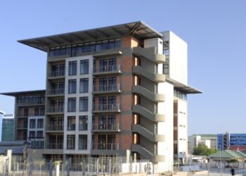 BUILDING2 - The Brief | Namibia's Leading Business & Financial News Modern six-story office building with exterior curved staircases on the right, brick and concrete façade, and large glass windows against a clear blue sky.