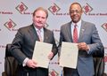 Two businessmen in suits pose with documents at a Bank of Namibia event backdrop.