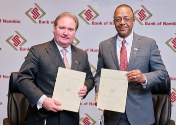 Two businessmen in suits pose with documents at a Bank of Namibia event backdrop.