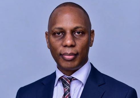 Andrew Njeru - The Brief | Namibia's Leading Business & Financial News Professional headshot of a man in a navy suit and plaid tie against a light blue backdrop, neutral expression.