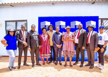 WhatsApp Image 2026-10-14 at 61108 PM - The Brief | Namibia's Leading Business & Financial News Ten people stand in a line outdoors, smiling, in front of a blue 'Buy a Brick' backdrop at a community event.