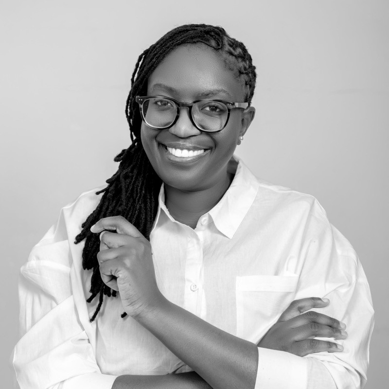 Smiling woman with glasses and braids in a white button-down shirt, facing the camera in a portrait.