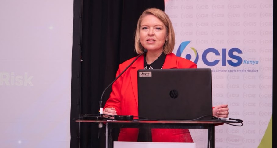Karen Jansen van Vuuren - The Brief | Namibia's Leading Business & Financial News Woman in a red blazer delivering a talk at a podium with a laptop on stage at a conference.