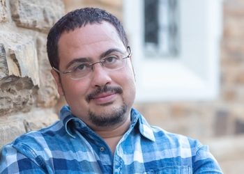 Berit Platt - The Brief | Namibia's Leading Business & Financial News Man with short dark hair and glasses leaning against a stone wall outdoors, wearing a blue plaid shirt.