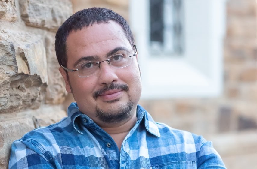Berit Platt - The Brief | Namibia's Leading Business & Financial News Man with short dark hair and glasses leaning against a stone wall outdoors, wearing a blue plaid shirt.
