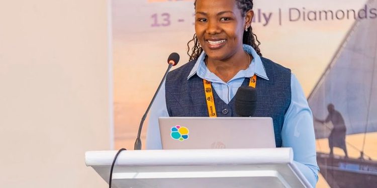 Woman speaker at a podium with a laptop and microphone, presenting at a conference with a 'Digital Transformation' banner in the background.