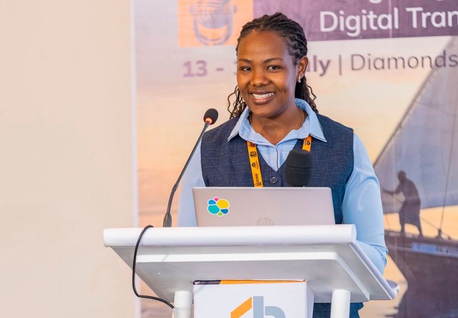 chritine waita - The Brief | Namibia's Leading Business & Financial News Woman speaker at a podium with a laptop and microphone, presenting at a conference with a 'Digital Transformation' banner in the background.