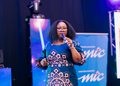 WhatsApp Image 2026-10-19 at 122531 - The Brief | Namibia's Leading Business & Financial News Black woman with glasses speaks into a handheld microphone on stage, wearing a teal patterned dress with a blue backdrop.