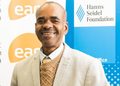 WhatsApp Image 2026-10-19 at 140652 - The Brief | Namibia's Leading Business & Financial News Smiling man in a beige blazer and tan sweater at a formal event, with banners for the Hanns Seidel Foundation in the background.