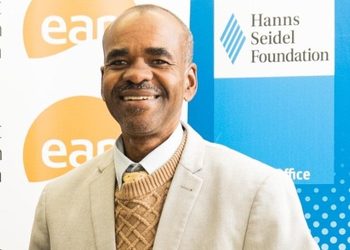 WhatsApp Image 2026-10-19 at 140652 - The Brief | Namibia's Leading Business & Financial News Smiling man in a beige blazer and tan sweater at a formal event, with banners for the Hanns Seidel Foundation in the background.