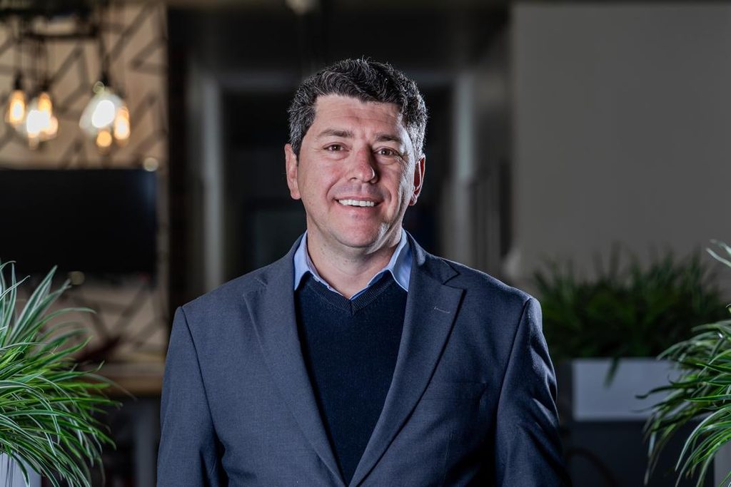 WhatsApp Image 2026-10-19 at 150912 - The Brief | Namibia's Leading Business & Financial News Portrait of a smiling man in a blue shirt and navy blazer in a modern office with plants nearby.