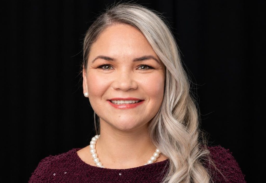 Alovise Frey - The Brief | Namibia's Leading Business & Financial News Smiling woman with pearly necklace and pearl earrings, wearing a burgundy sweater against a black background.