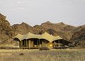 tented lodge - The Brief | Namibia's Leading Business & Financial News Desert camp with a row of beige canvas tents set on a platform against rocky desert hills at dusk.