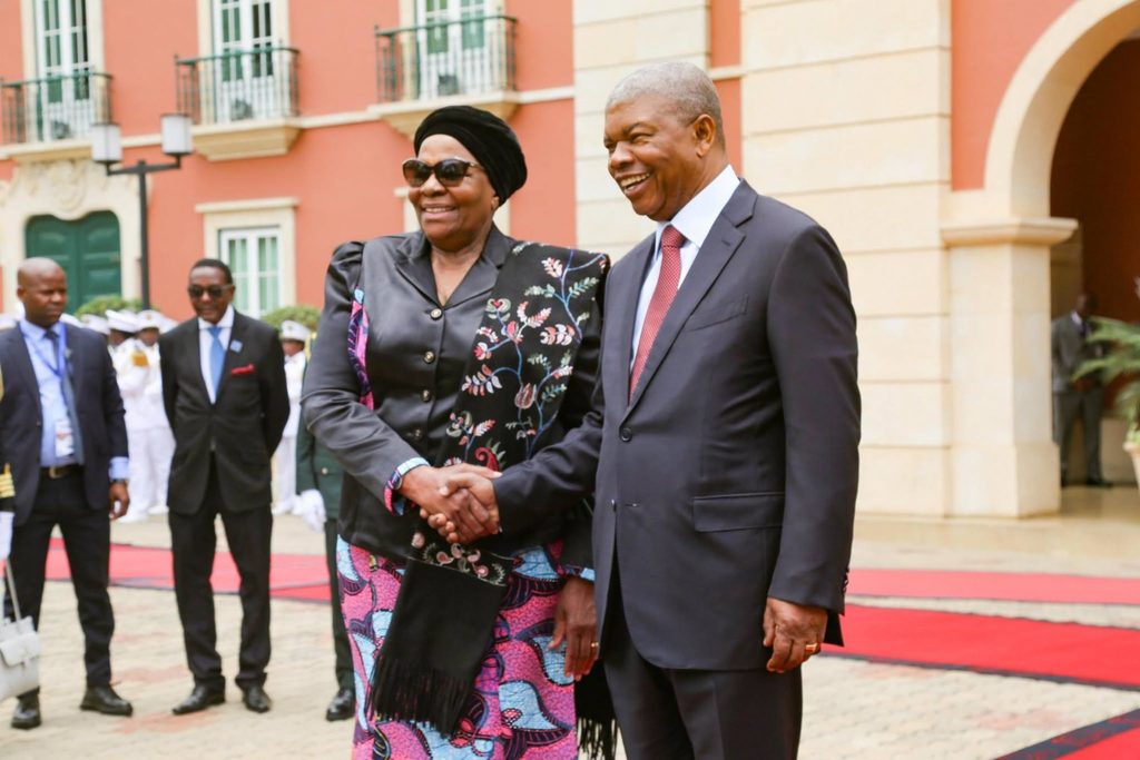 WhatsApp Image 2026-10-21 at 45240 PM - The Brief | Namibia's Leading Business & Financial News Two formally dressed leaders shake hands and smile on a red carpet outside a pastel building.