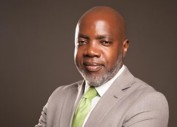 Professional headshot: bald man in a gray suit and lime green tie, smiling slightly.
