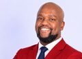 Professional headshot of a smiling man in a red blazer and navy tie against a light background.