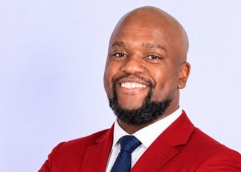 Moses Gaweseb - The Brief | Namibia's Leading Business & Financial News Professional headshot of a smiling man in a red blazer and navy tie against a light background.