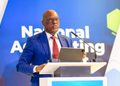 TOM ALWEENDO3 - The Brief | Namibia's Leading Business & Financial News Man in a blue suit delivering a speech at a podium with two microphones, blue backdrop behind him.