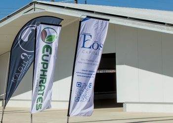 Three vertical banners outside a modern white building; left banner is dark with a logo, center banner has green vertical text, right banner reads 'EOS CAPITAL' with a QR code.