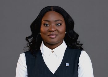 Professional woman in a white collared shirt and pinstripe vest, facing the camera against a gray background.