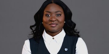 Professional woman in a white collared shirt and pinstripe vest, facing the camera against a gray background.