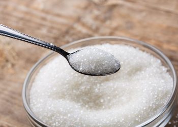 WHITE SUGAR - The Brief | Namibia's Leading Business & Financial News Spoonful of white granulated sugar held over a jar of sugar on a wooden surface