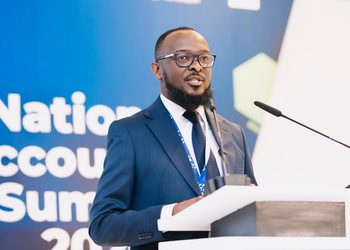 Man in a blue suit and glasses speaks at a podium during a National Accounts Summit, with a blue backdrop behind him.
