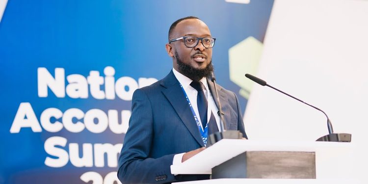 Man in a blue suit and glasses speaks at a podium during a National Accounts Summit, with a blue backdrop behind him.