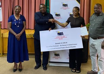 WhatsApp Image 2026-10-23 at 53502 PM - The Brief | Namibia's Leading Business & Financial News Award ceremony scene: two men shake hands as a woman presents a large check from the Livestock and Livestock Products Board of Namibia, with a banner behind them.